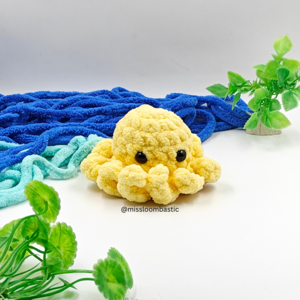 Handmade yellow crochet amigurumi octopus plush toy with cute black eyes, displayed with ocean-inspired background
